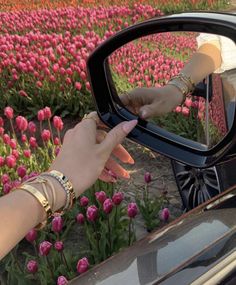 a woman's hand on the side mirror of a car in front of a field of tulips