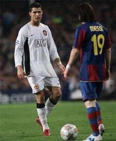 two men playing soccer on a field with fans in the stands and one man standing next to the ball