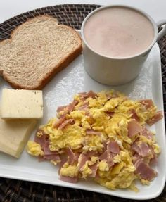 a white plate topped with eggs, ham and cheese next to a cup of coffee