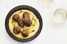 meatballs and mashed potatoes are served in a black bowl next to two glasses