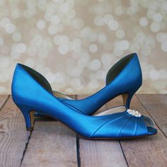 a pair of blue high heeled shoes with pearls on the toe, sitting on a wooden floor