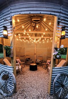 an outdoor seating area with chairs and lights on the roof, surrounded by metal barrels