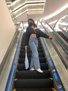 a woman wearing a face mask and jeans is riding an escalator down the stairs