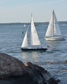 three sailboats are sailing in the water near some rocky shorelines and large rocks