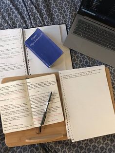 an open notebook and pen sitting on top of a bed next to a laptop computer