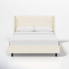 a bed with white linens and pillows on it, against a plain wall background