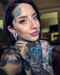 a woman with tattoos and piercings on her face is posing for the camera,