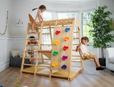 two children playing on a wooden climbing frame in a living room with white walls and wood flooring