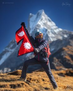 a person standing on top of a grass covered hill holding a red and white flag