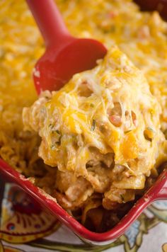 a red casserole dish filled with chicken and cheese, topped with a red spatula