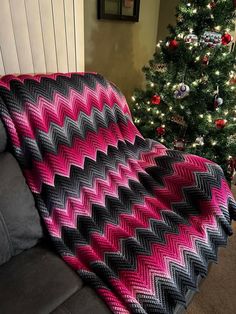 a pink and black blanket sitting on top of a couch next to a christmas tree