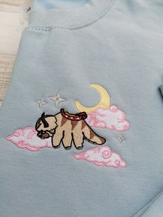 a blue shirt with a small dog on it's chest and clouds in the background