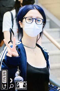 a woman with blue hair wearing a face mask and making the peace sign while standing in front of stairs