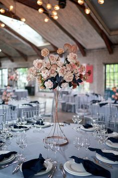 an elegant centerpiece with pink roses in a tall vase sits atop a table set for dinner