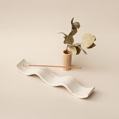 a white vase with a plant in it next to a wooden stick