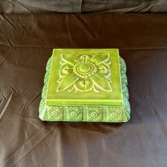 a green ceramic box sitting on top of a black cloth covered tablecloth with an intricate design