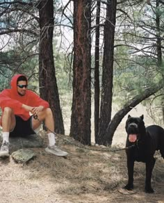 a man sitting on top of a rock next to a black dog in the woods