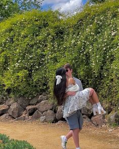 a man carrying a woman on his back walking down a dirt road next to bushes