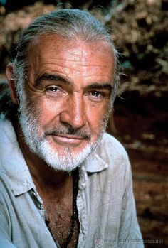 an older man with white hair and beard wearing a gray shirt is smiling at the camera