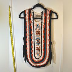 a crocheted vest hanging on a wall next to a ruler