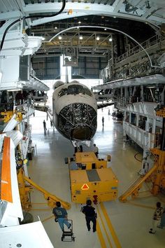 an airplane is being worked on in a hangar with workers around it and people standing near the plane