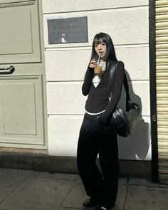 a woman standing on the sidewalk drinking from a cup