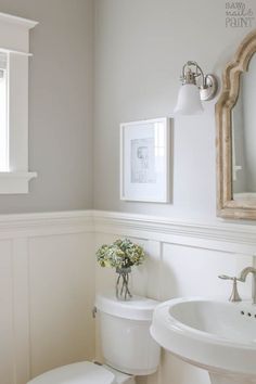 a white toilet sitting next to a sink in a bathroom under a framed painting on the wall