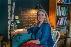 a woman sitting at a desk in front of a chalkboard