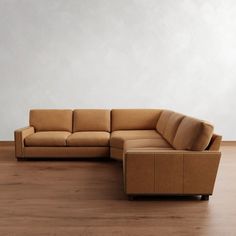 a brown leather couch sitting on top of a wooden floor next to a white wall