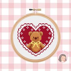 a cross stitch heart with a teddy bear holding a bow in it's paws