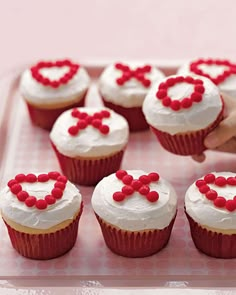 cupcakes decorated with white frosting and red candies are being held by a hand