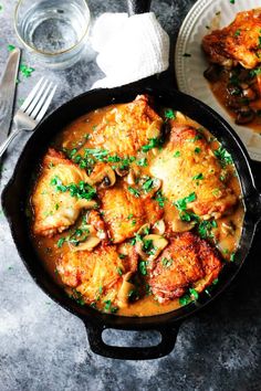 a skillet filled with chicken and mushrooms on top of a table next to silverware