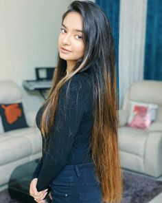 a woman with long hair standing in front of a living room couch and chair, looking at the camera