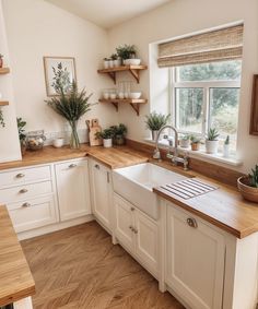 a kitchen with white cabinets and wooden counter tops, potted plants on the window sill