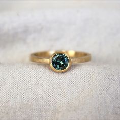 Dainty yellow gold ring featuring a round bi-colour green/blue sapphire with a thin halo of gold around the stone. Green Round Stone Fine Jewelry, Handmade Yellow Gold Fine Gemstones, Green 14k Gold Gemstones With Accent Stones, Elegant Green Round Gemstones, Green Sapphire Ring