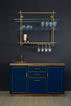 a kitchen with blue cabinets and gold trim on the shelves, wine glasses hanging from the wall