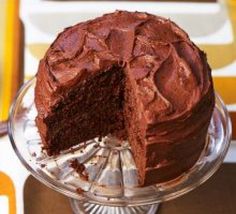 a chocolate cake with one slice taken out of it on a glass platter next to a yellow and white striped tablecloth