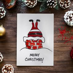 a christmas card with a santa hat on it and pine cones in the background, along with other holiday decorations