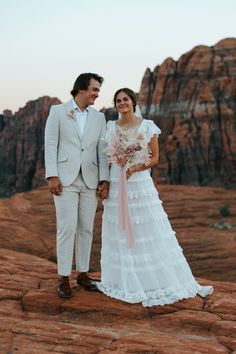 a bride and groom standing on top of a rock formation in the desert at sunset