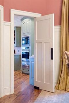 an open door leading to a kitchen with pink walls and wood floors in the background