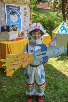 a young boy in space suit holding up a paper airplane and cardboard cutout on grass