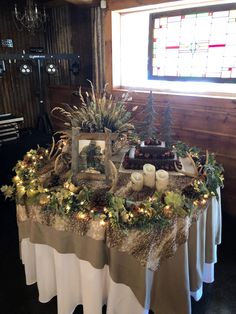 the table is set with candles, pine cones and greenery on it for christmas