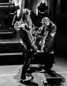 two men in skeleton costumes on stage with one holding a guitar and the other standing behind him