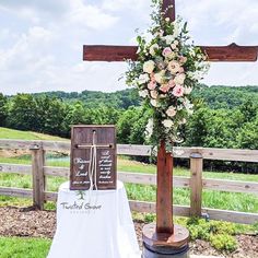 a wooden cross sitting on top of a field next to a table covered in flowers