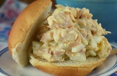 a sandwich filled with meat and potato salad on a plate next to a blue bowl