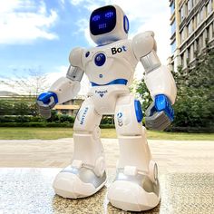 a white robot standing on top of a table next to a tall building with lots of windows