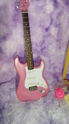 a pink electric guitar sitting on top of a purple fur covered floor next to a toy mouse