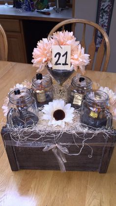 a wooden box with jars and flowers in it sitting on top of a wood table