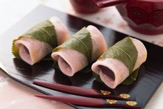 three pieces of sushi on a black plate with chopsticks and sauce in the background