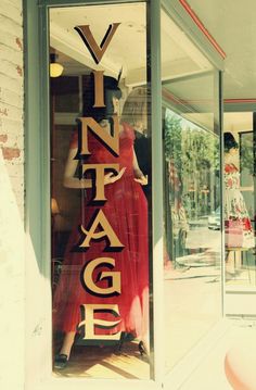 a woman in a red dress is standing behind a window with the words vintage on it